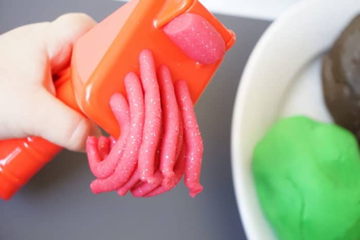 rote Knoblauchpresse aus der pinke Glitzerknete rausgedrückt wird