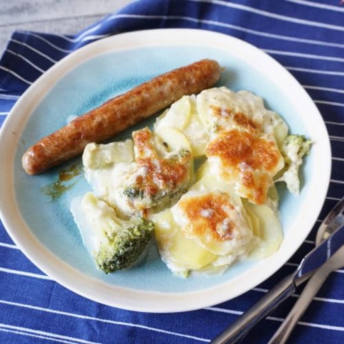 Teller mit knsurpig überbackenen Kartoffelgratin mit Brokkoli und Käse, dazu Bratwurst