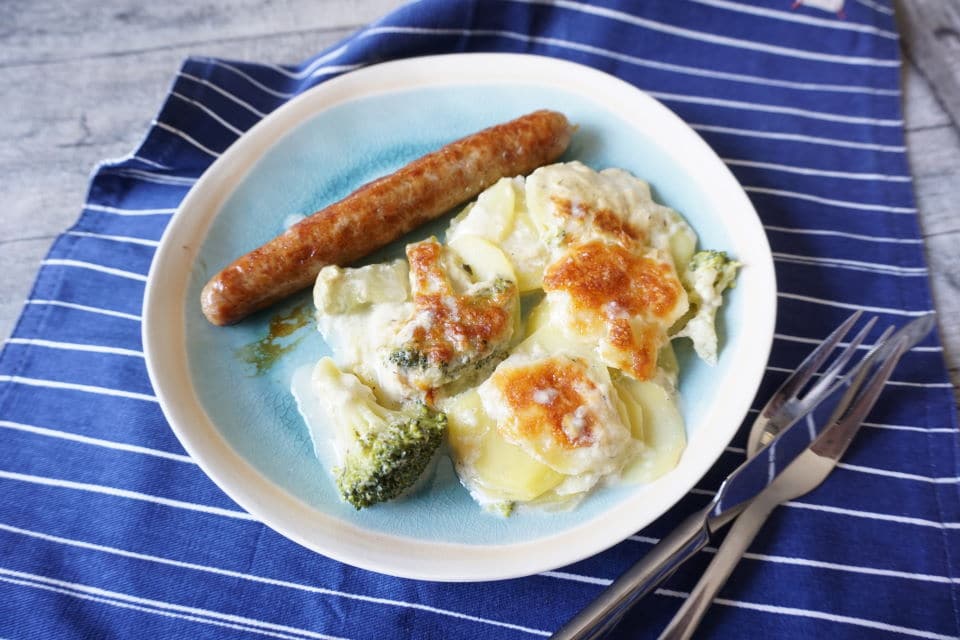 Teller mit knsurpig überbackenen Kartoffelgratin mit Brokkoli und Käse, dazu Bratwurst