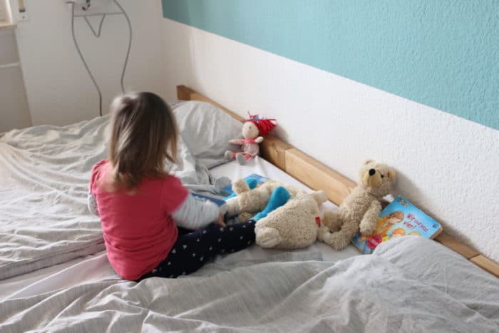 Mädchen sitzt im Familienbett mit Kuscheltieren, Teddy und Puppe