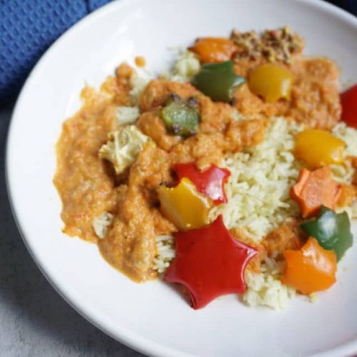 weißer Teller mit Reis und oraangefarbener paprika Zucchini Soße und Sternen aus Gemüse ausgestochen - Gemüsesoße für Kinder