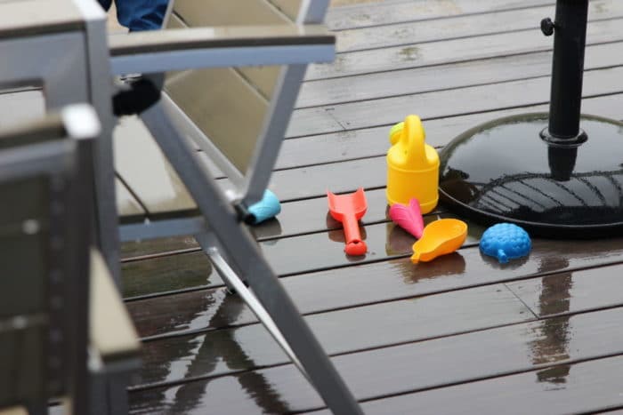 Sandspielsachen liegen im Regen auf der Terasse: Schaufel, Gießkanne und Förmchen