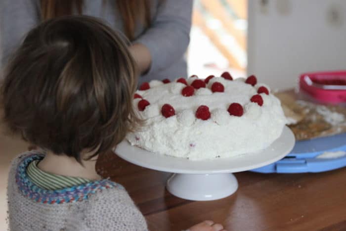 Kinderkopf von hinten fotografiert, Mädchen schaut auf die Raffaellotorte mit Himbeeren